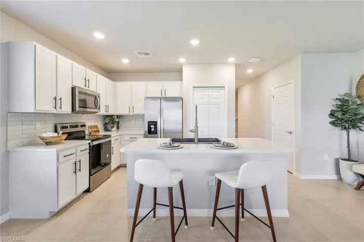 The kitchen features a large quartz island with quartz composite sink and updated faucet,  white cabinetry with black pulls & Italian tile backsplash
