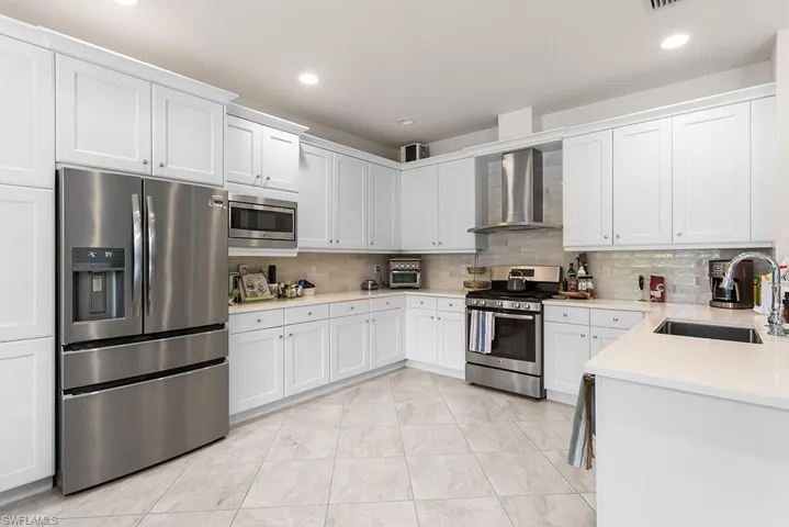 Kitchen featuring white cabinets, sink, wall chimney exhaust hood, tasteful backsplash, and stainless steel appliances