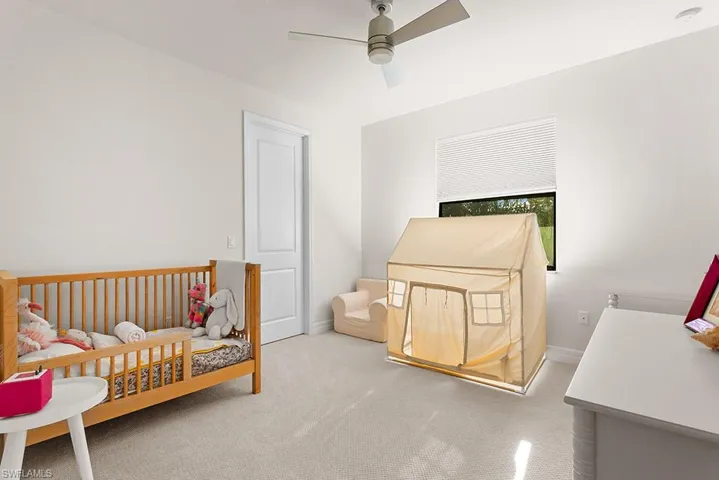 Carpeted bedroom featuring a nursery area and ceiling fan
