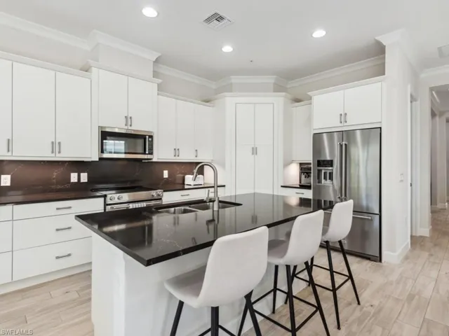 Kitchen with decorative backsplash, appliances with stainless steel finishes, sink, white cabinetry, and an island with sink