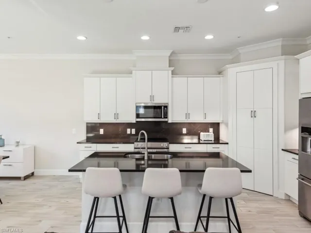 Kitchen featuring a kitchen bar, a center island with sink, white cabinets, and appliances with stainless steel finishes