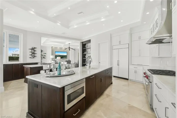 Kitchen featuring ornamental molding, light stone countertops, built in appliances, ventilation hood, and glass fronted cabinets