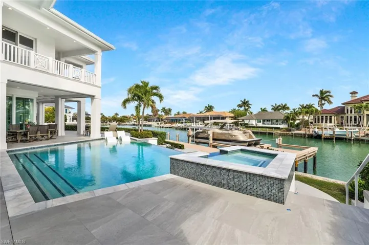 View of swimming pool with an infinity pool, an in-ground hot tub, patio surround, and a water view
