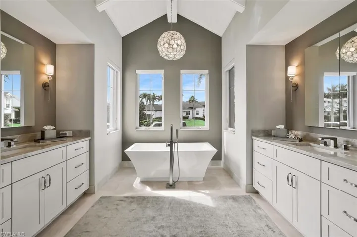 Bathroom with a chandelier, a soaking tub, two vanities, beam ceiling, and light tile patterned floors