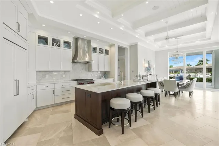 Kitchen featuring light stone countertops, a spacious island, pendant lighting, a kitchen bar, and glass insert cabinets