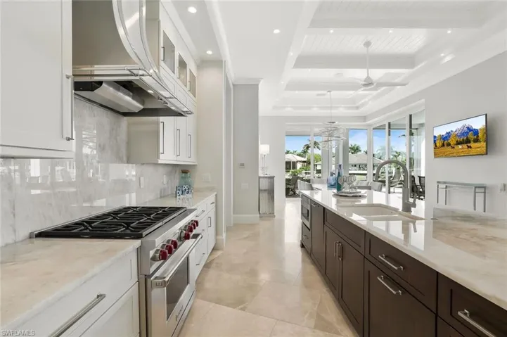 Kitchen featuring stainless steel appliances, light stone countertops, two tone cabinetry, glass fronted cabinets, and decorative light fixtures