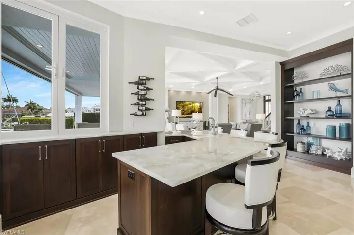 Kitchen featuring a breakfast bar area, recessed lighting, coffered ceiling, light stone countertops, and dark wood finish cabinets