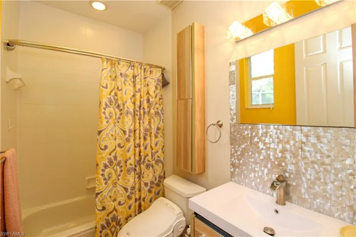 Full bathroom with toilet, backsplash, vanity, and shower / tub combo with curtain