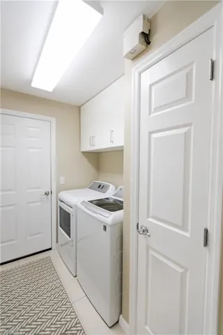 Clothes washing area featuring separate washer and dryer, light tile floors, and cabinets
