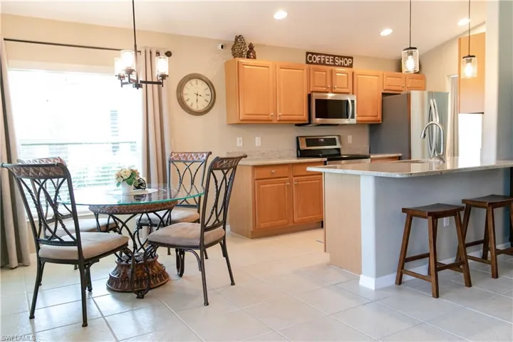 Kitchen with appliances with stainless steel finishes, decorative light fixtures, light tile flooring, and light stone counters