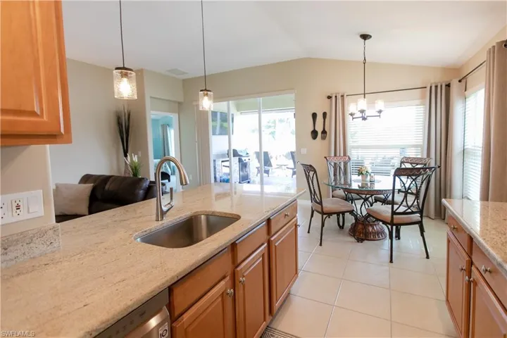 Kitchen with light stone countertops, decorative light fixtures, light tile flooring, sink, and lofted ceiling