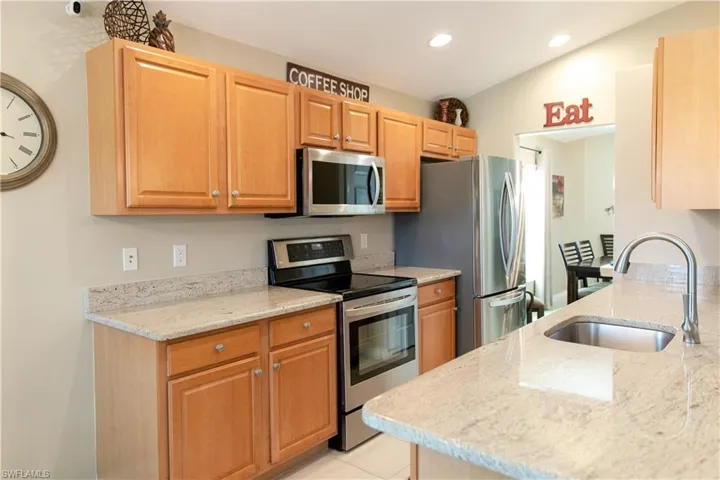 Kitchen with light stone countertops, lofted ceiling, stainless steel appliances, sink, and light tile floors