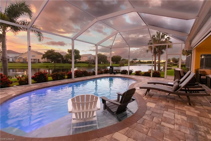 Pool at dusk with a patio, glass enclosure, and a water view