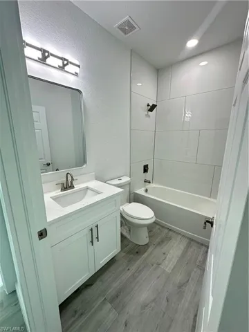 Full bathroom featuring hardwood / wood-style floors, vanity, toilet, and tiled shower / bath combo