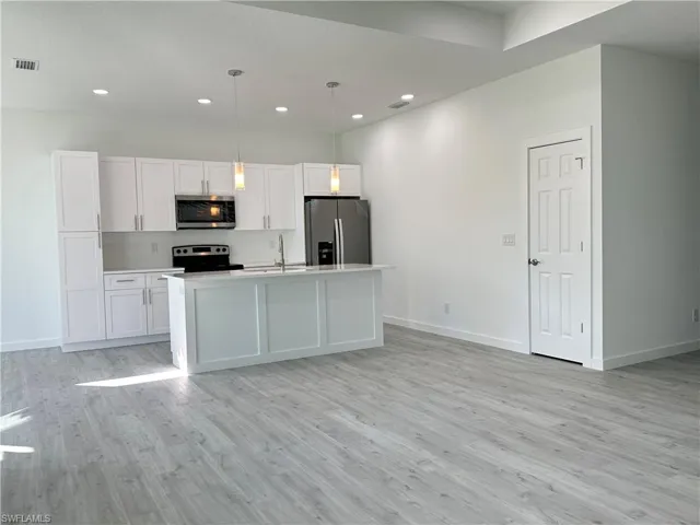 Kitchen with a center island with sink, white cabinetry, hanging light fixtures, and appliances with stainless steel finishes