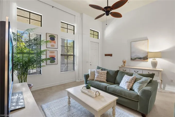Living room with light colored carpet, ceiling fan, and a high ceiling