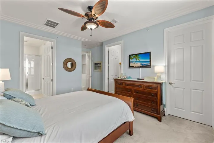 Carpeted bedroom with ornamental molding, ensuite bath, and ceiling fan