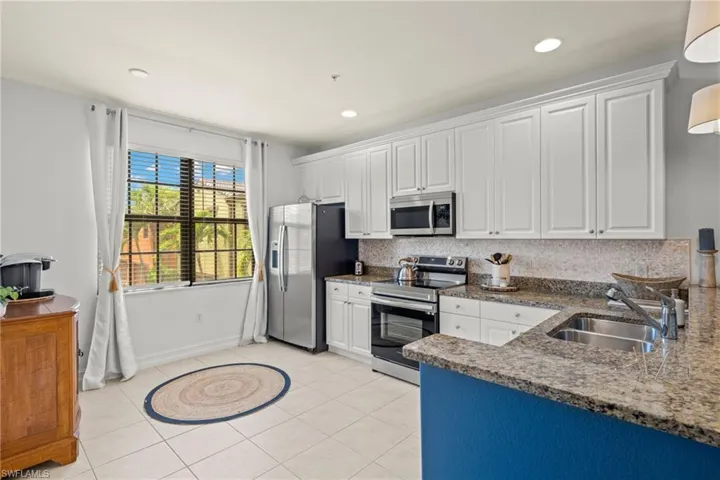 Kitchen featuring appliances with stainless steel finishes, white cabinetry, decorative backsplash, and sink