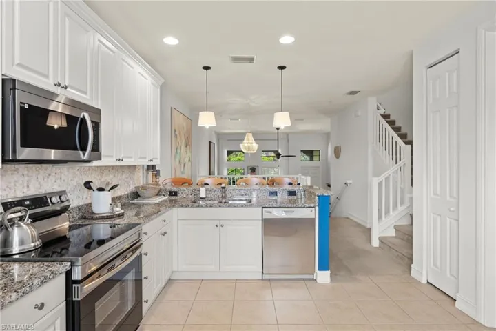 Kitchen with stainless steel appliances, kitchen peninsula, light stone counters, light tile patterned floors, and backsplash