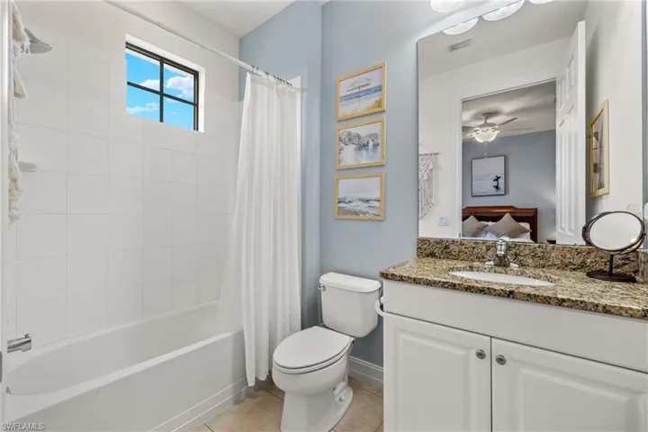 Full bathroom with shower / bathtub combination with curtain, tile patterned floors, toilet, vanity, and ceiling fan