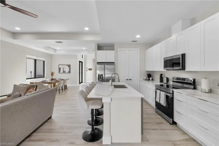 Bright kitchen featuring white shaker cabinetry, stainless steel appliances, a center island with countertop seating, and light wood-finish flooring