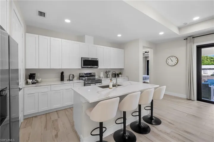 Contemporary kitchen featuring white shaker cabinetry, stainless steel appliances, and a central island with a waterfall countertop