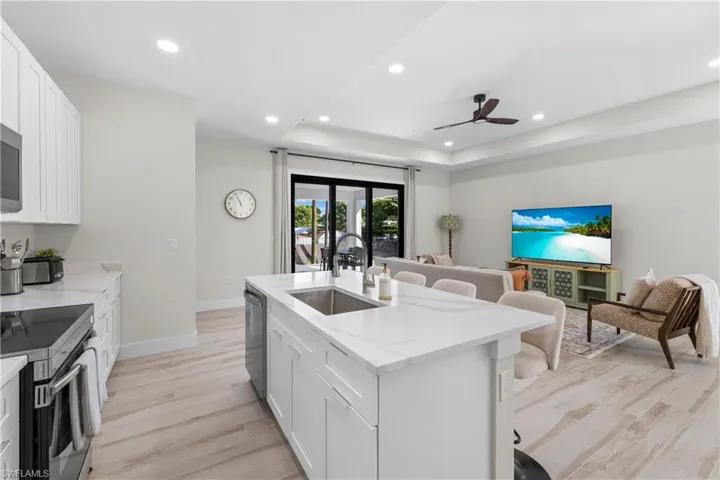 Modern kitchen island with an integrated sink, white cabinetry, quartz-finish countertops, stainless steel appliances, and light wood-finish flooring