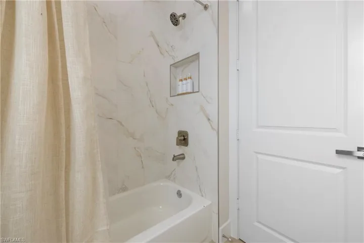 Bathtub and shower combination featuring a tiled surround with an integrated shower niche and brushed nickel fixtures