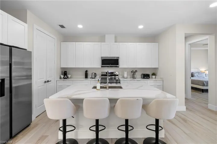 Gourmet kitchen featuring a large island with sink, white shaker cabinetry, stainless steel appliances, and wood-finish flooring