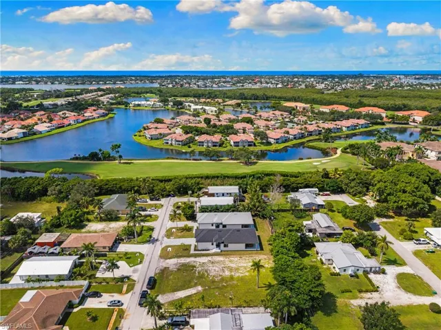 Aerial perspective showcasing the surrounding neighborhood, featuring a prominent body of water, extensive green spaces, and a distant ocean horizon