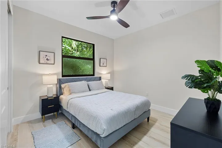 Bedroom featuring a black-framed window, wood-finish flooring, white baseboards, and a dark-toned ceiling fan with integrated lighting