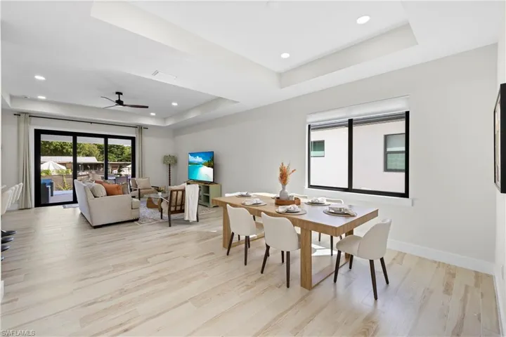 Open-concept living space with light wood-finish flooring, recessed lighting, and a tray ceiling