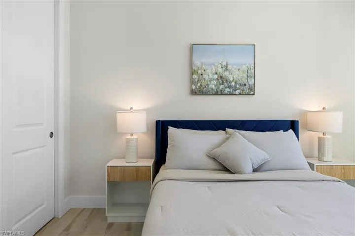 Light-toned bedroom featuring wood-finish flooring, white baseboards, and a white interior door