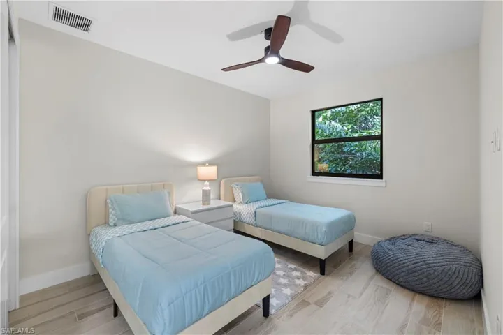 Neutral-toned interior room featuring wood-finish flooring, a window with exterior foliage, and an overhead ceiling fan with integrated lighting