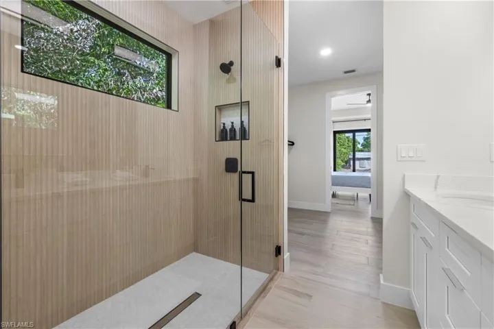 Modern shower enclosure featuring a glass door, textured tile walls, and a linear drain