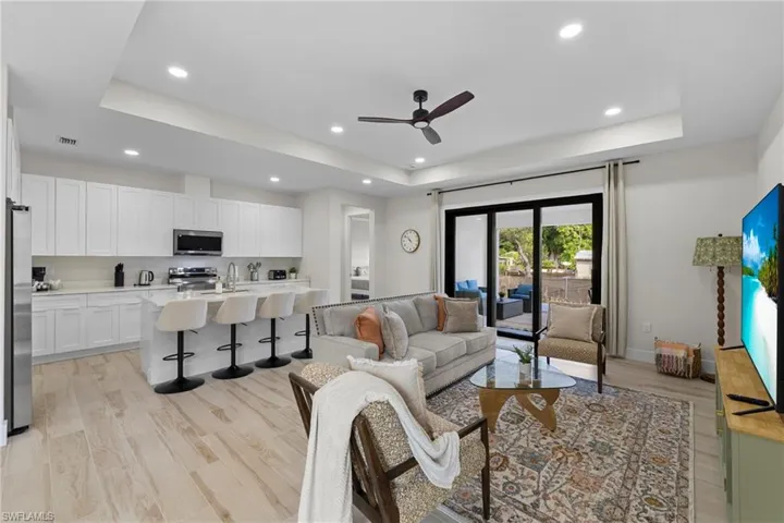 Expansive open-concept living space featuring wood-finish flooring, a contemporary kitchen with white cabinetry, a large kitchen island with seating, a ceiling fan, and sliding glass doors leading to an outdoor area