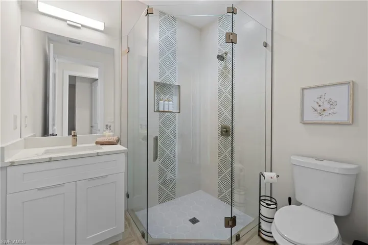 Glass-enclosed corner shower with patterned accent tiling and a built-in niche