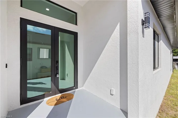 Double glass-panel entry doors with black frames, transom window, and white stucco exterior