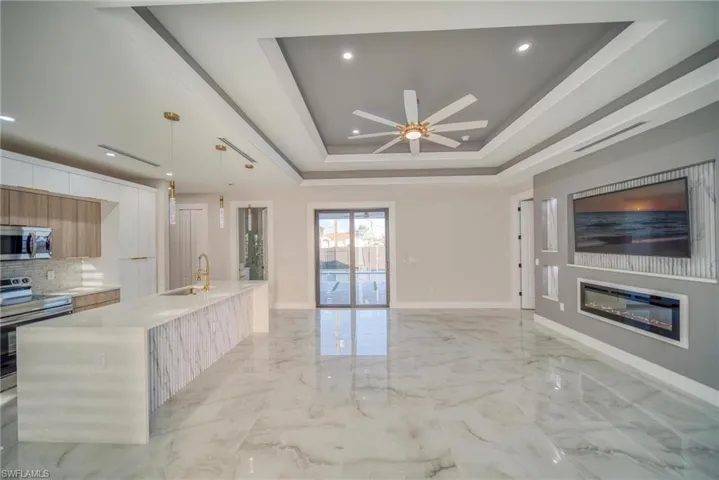 Kitchen featuring a large island with sink, hanging light fixtures, a tray ceiling, appliances with stainless steel finishes, and ceiling fan