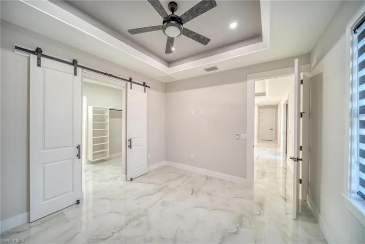 Unfurnished bedroom with multiple windows, a barn door, a tray ceiling, and ceiling fan