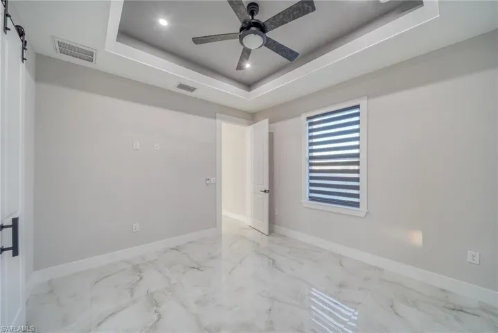 Empty room featuring a barn door, a tray ceiling, and ceiling fan