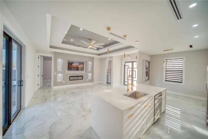 Kitchen featuring dishwasher, a kitchen island with sink, a tray ceiling, sink, and pendant lighting