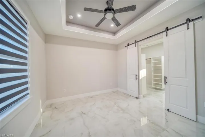 Unfurnished bedroom featuring a barn door, a raised ceiling, and ceiling fan