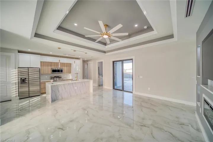 Kitchen with an island with sink, white cabinets, decorative light fixtures, a raised ceiling, and appliances with stainless steel finishes