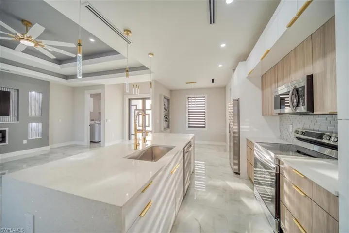 Kitchen with sink, stainless steel appliances, decorative light fixtures, white cabinets, and a kitchen island with sink