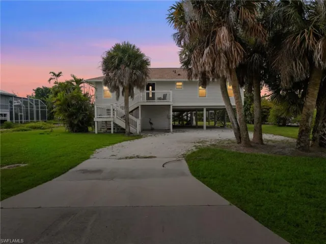 Coastal home with a carport, stairway, driveway, a deck, and a front lawn