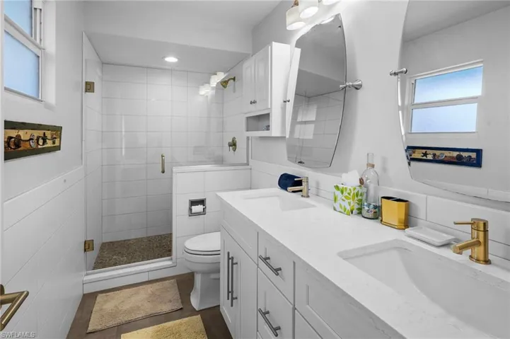 Full bath with healthy amount of natural light, double vanity, a stall shower, and dark tile patterned flooring