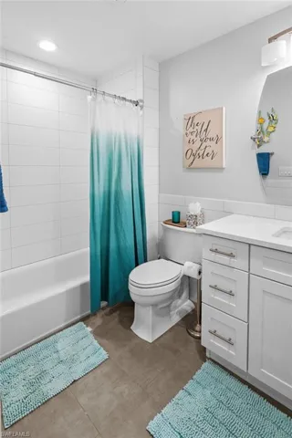 Bathroom with vanity, shower / bath combo with shower curtain, wainscoting, and tile walls