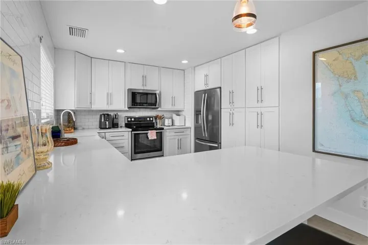 Kitchen featuring a peninsula, stainless steel appliances, light stone counters, white cabinetry, and recessed lighting