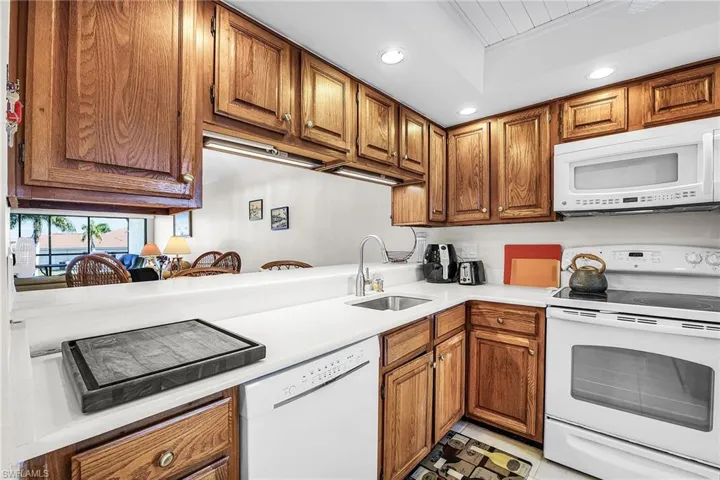 Kitchen featuring white appliances, recessed lighting, brown cabinetry, and light countertops